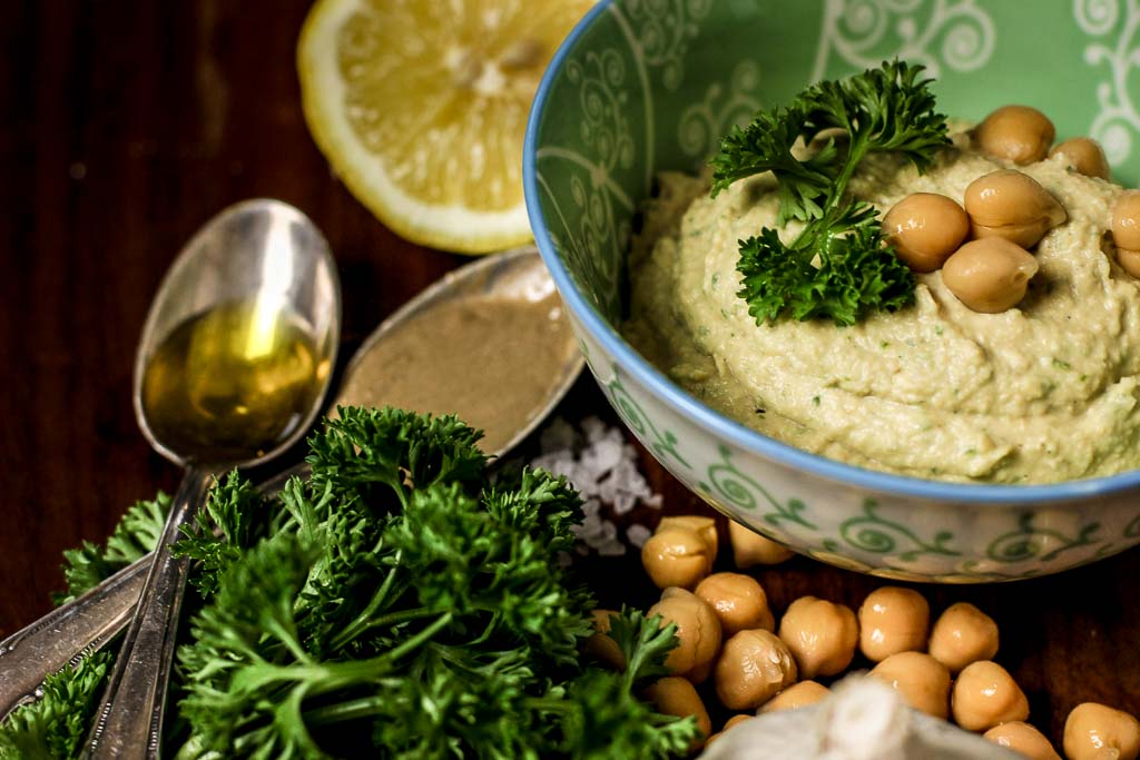 Grüner Hummus dekoriert mit Petersilie, Kichererbsen, Zitrone. Öl und Tahin